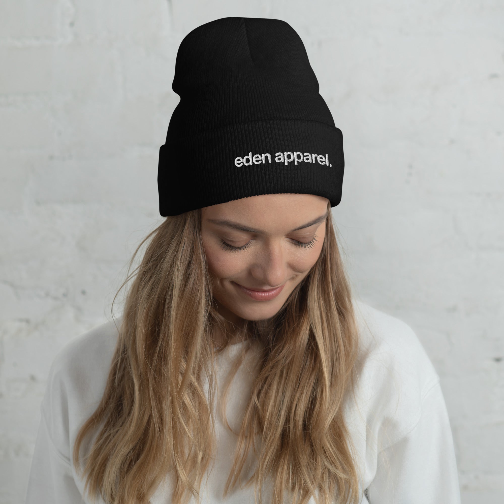 Woman wearing a black beanie with 'eden apparel' logo against a light gray background
