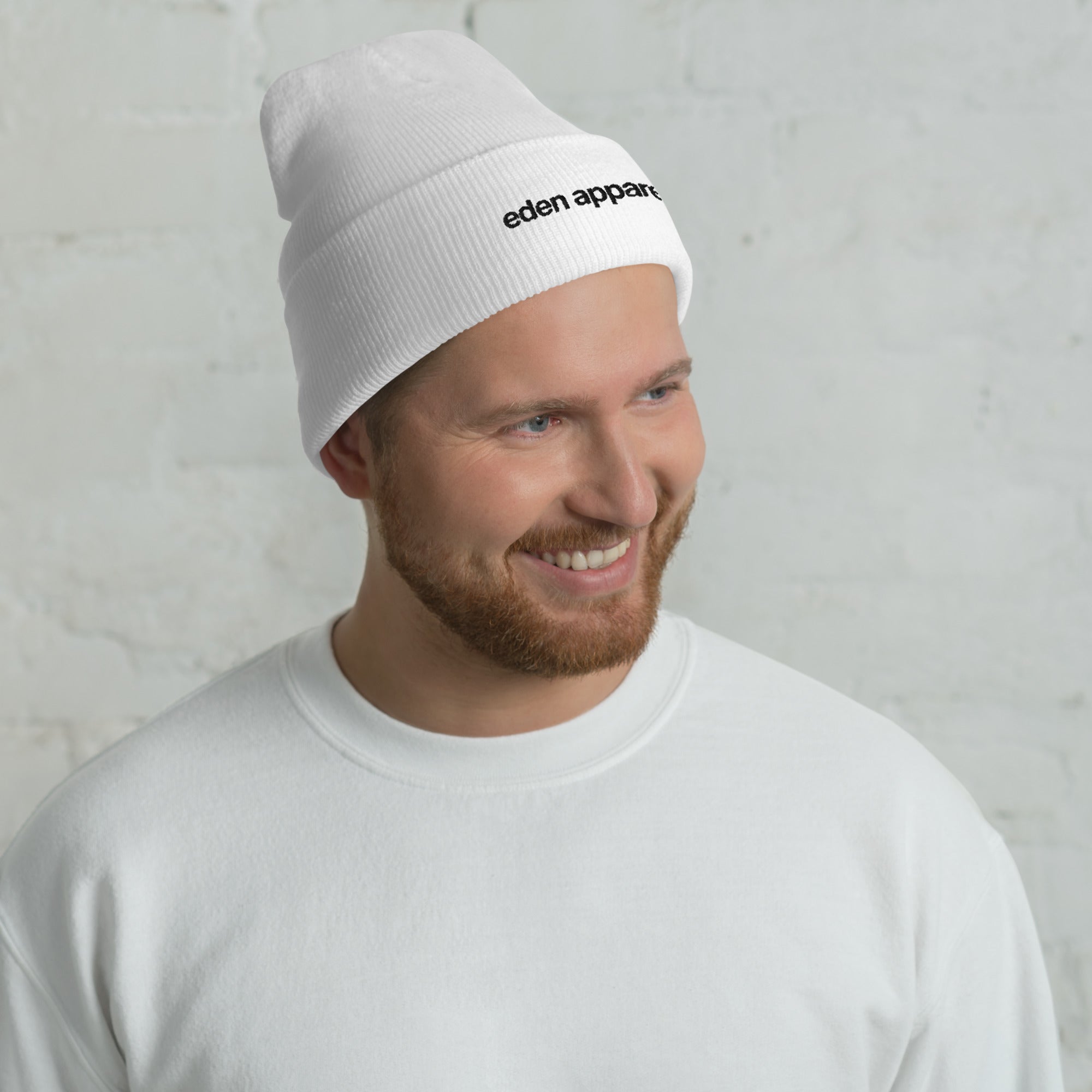 Man wearing a white beanie with 'eden apparel' logo against a light gray background